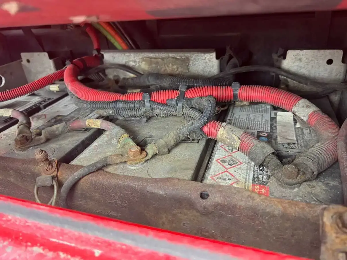 The battery box of a red truck opened up, cables and terminals exposed