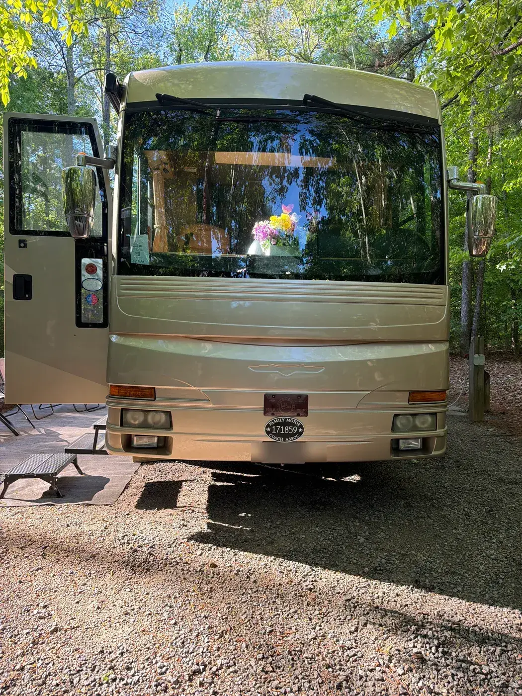 The front of a Class A motor home parked at a campsite with its entry door open