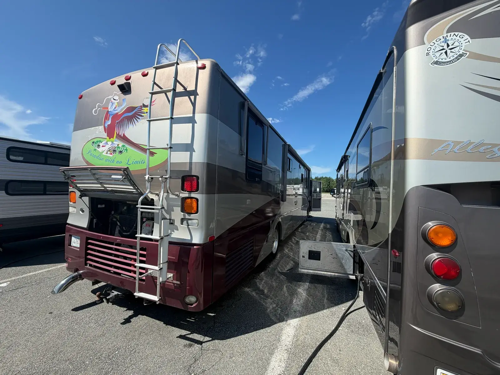 Two Class A motor homes parked side by side, the nearer one with its rear engine bay open for service