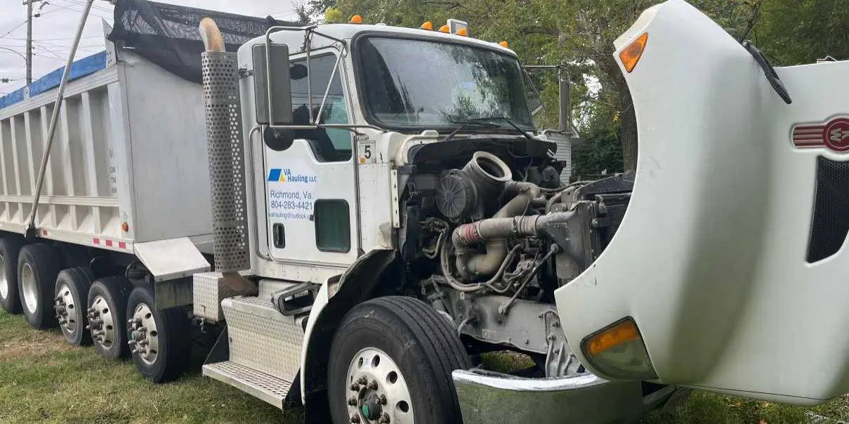 A Peterbilt dump truck lettered for a Richmond hauling company, hood open for engine work