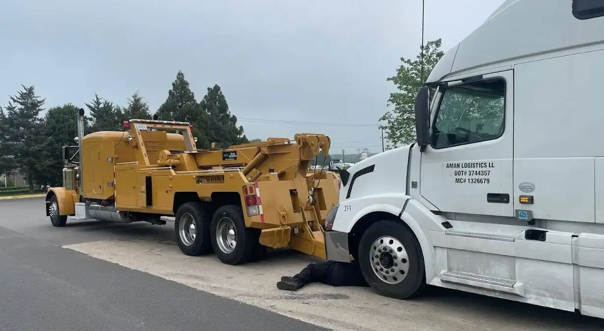 The Tri City wrecker hooked to a white Volvo sleeper while a technician works underneath it