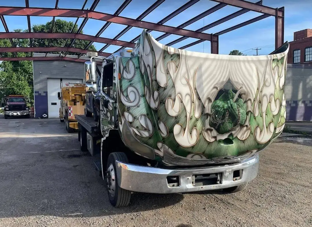 A custom-painted truck on a flatbed in the Tri City yard, with the company's wrecker parked behind it