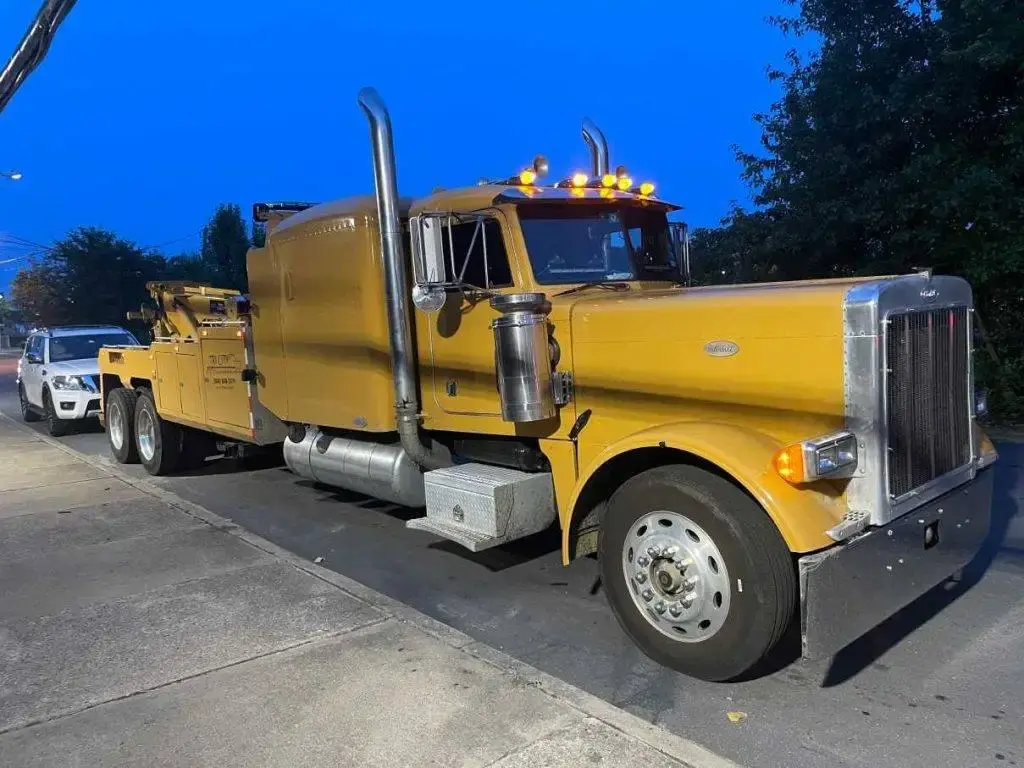Tri City's yellow Peterbilt wrecker hitched to a vehicle at dusk